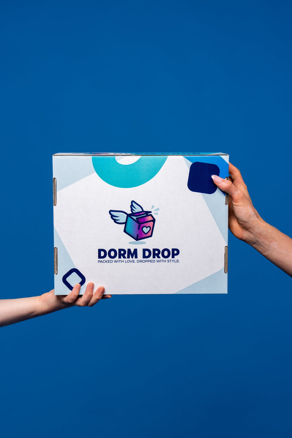 Two hands holding a white Dorm Drop shipping box with the company logo and tagline against a bright blue background.
