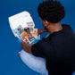 A college student in a black tee opens a Dorm Drop care package box, overhead view