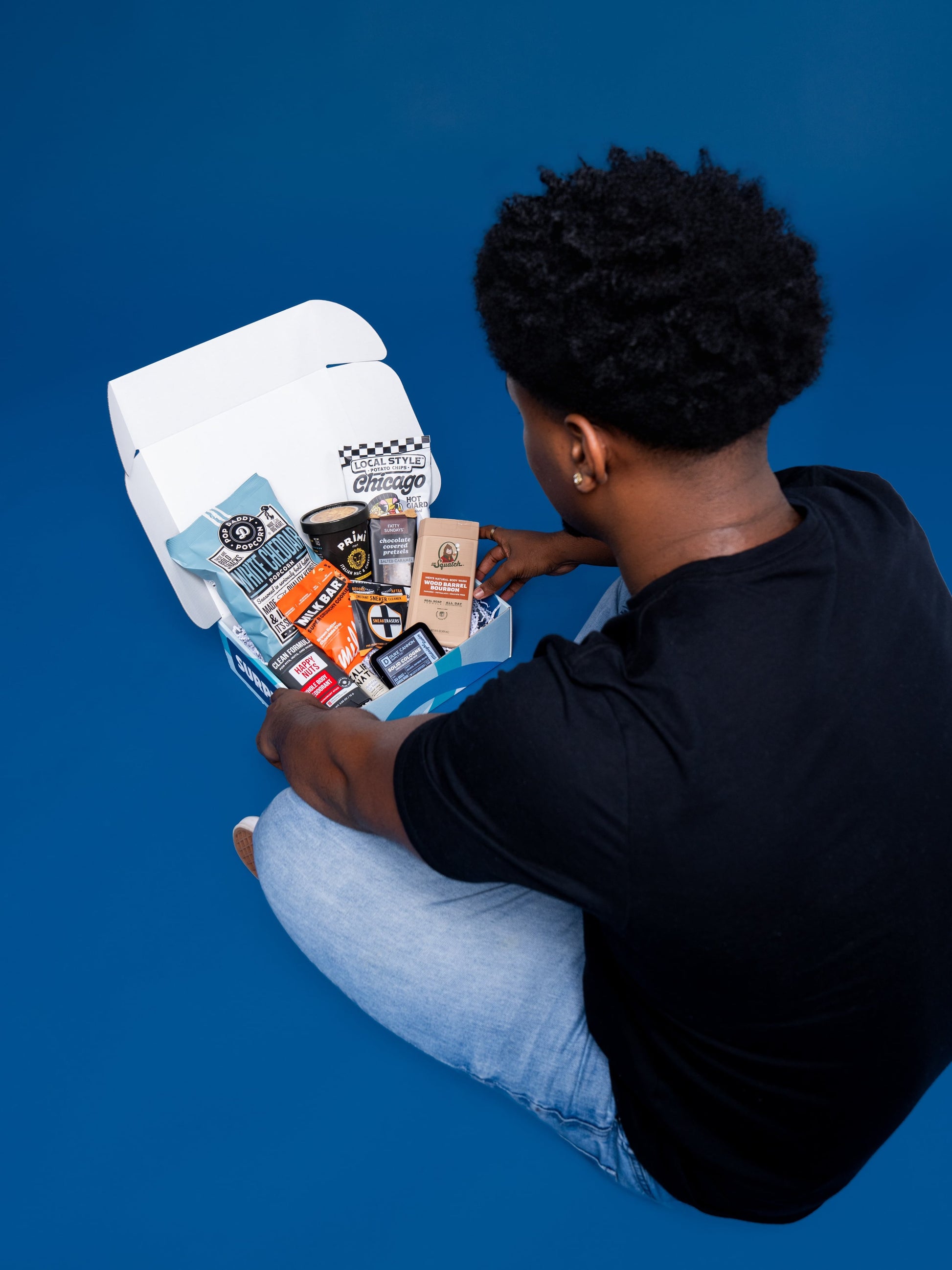 A college student in a black tee opens a Dorm Drop care package box, overhead view