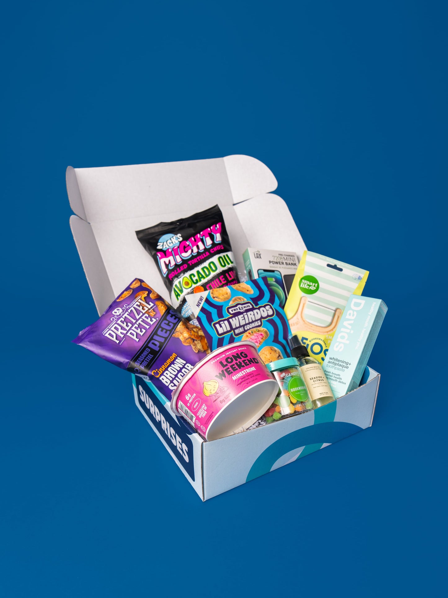 An open Dorm Drop box on a blue background, packed with snacks, a power bank, toothpaste and dorm toiletries